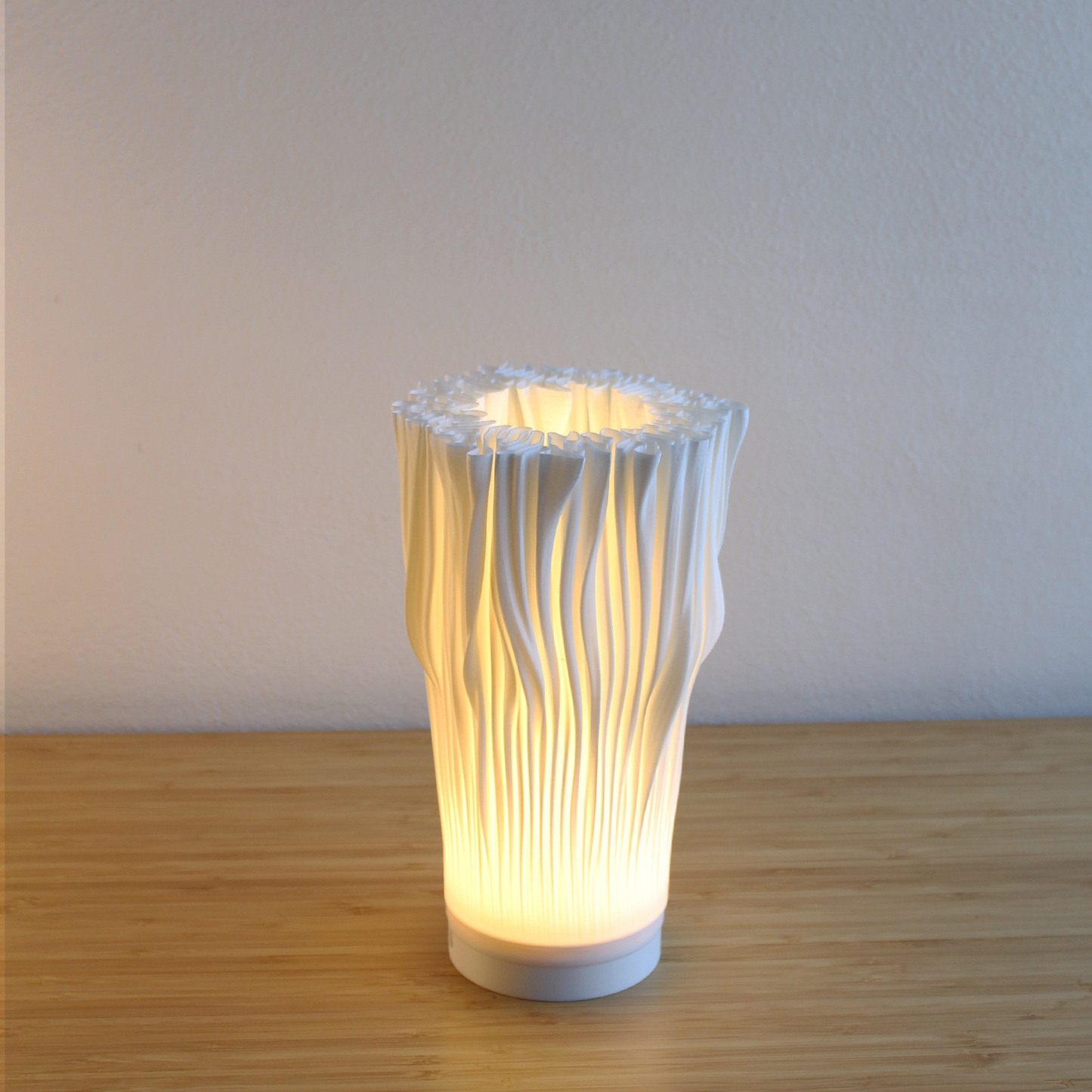 Illuminated Portable Coral Lamp on a wooden table. Emitting a warm, dimmable 3000K glow, emphasizing its flowing, textured shade.