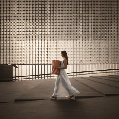 Woman in a white dress holding a Chocolate Dune Side Table against a textured wall.