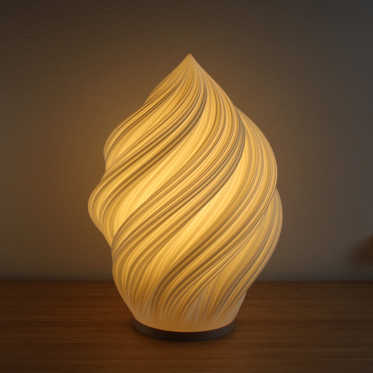 Soft Serve Lamp in white, 3D-printed with swirling ice cream–inspired design, glowing warmly on a side table.