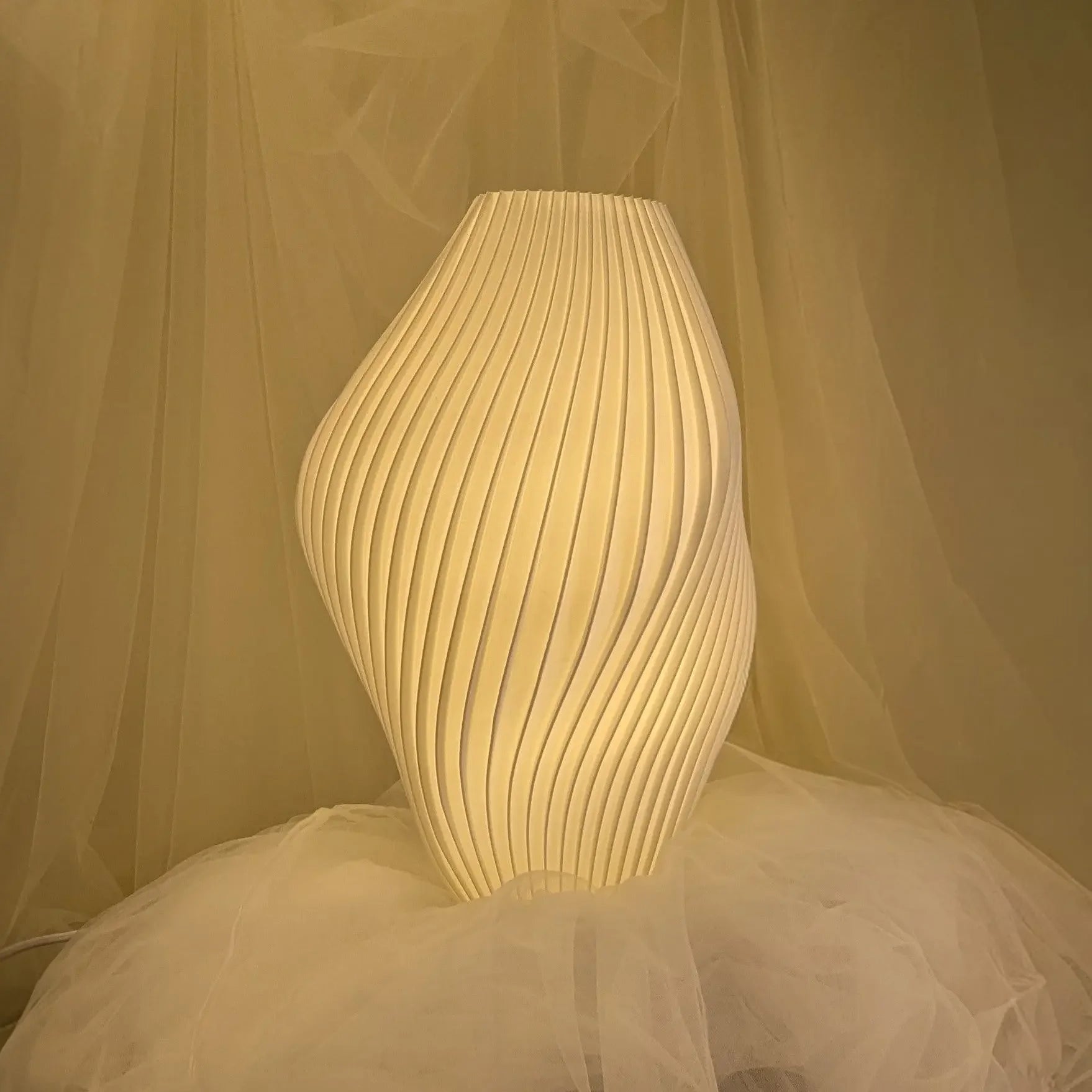 White Namami Pleat textured table lamp with soft glow against a sheer curtain background