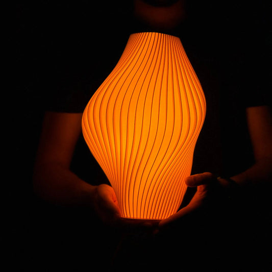 Orange textured Namami Pleat Mandarin lamp held in hands against a dark background