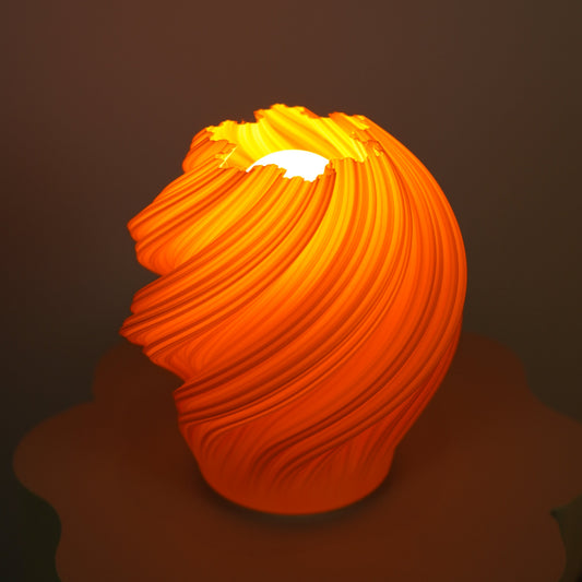 An orange sculptural lamp with a ribbed, shell-like surface glowing warmly, placed on a matching orange flower-shaped base against a dark brown background.