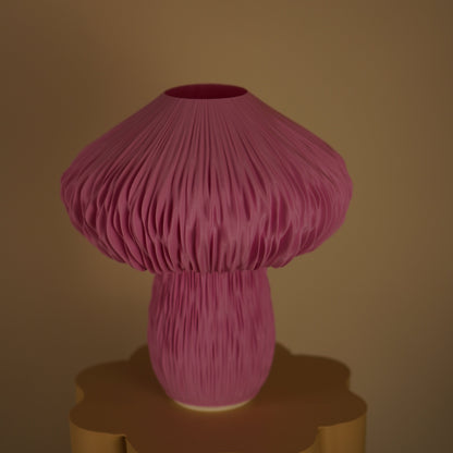 A mushroom-shaped pink pleated table lamp with a textured, accordion-like fabric shade and matching base, displayed on a sculptural gold pedestal against a warm beige background.