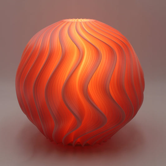 Close-up studio shot of the Flamingo Orb Lamp with flowing wave geometry illuminated in bright orange against a neutral backdrop.