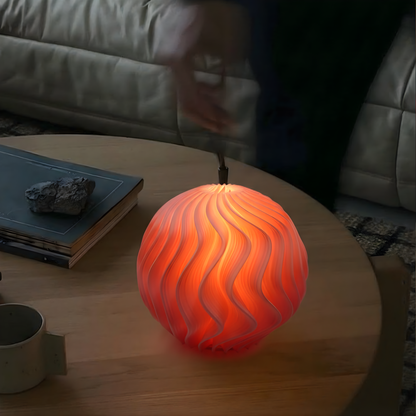 Glowing orange Orb Lamp placed on a round wooden table, showing its sculptural wave texture and warm ambient light