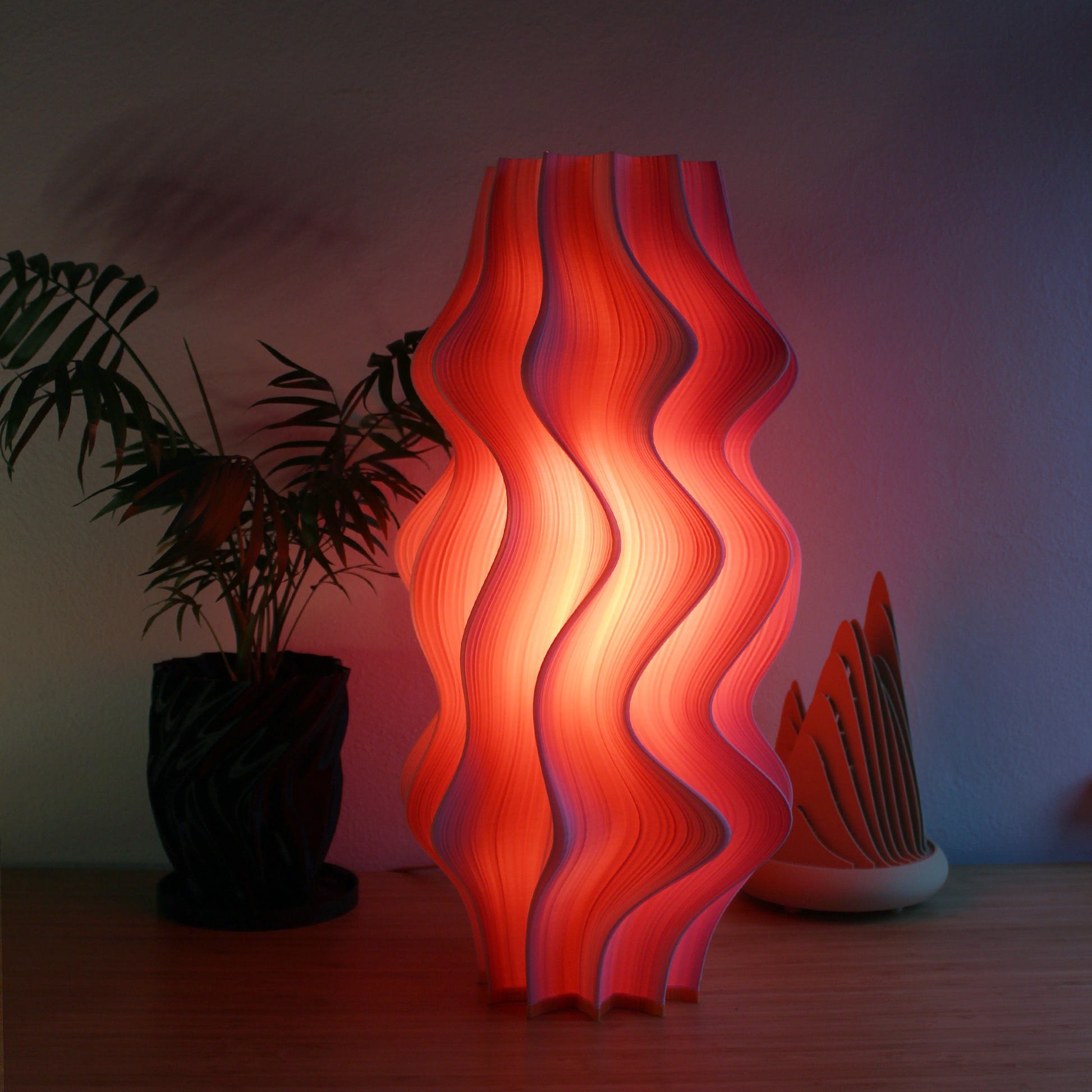 Wavy Flamingo Iris Namami lamp on a table with plants in the background