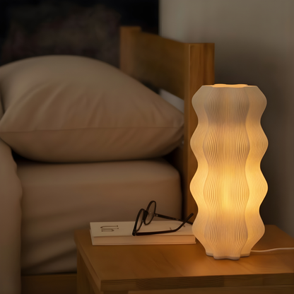 Harp Lamp by Namami on a bedside table with pillows and a book in the background