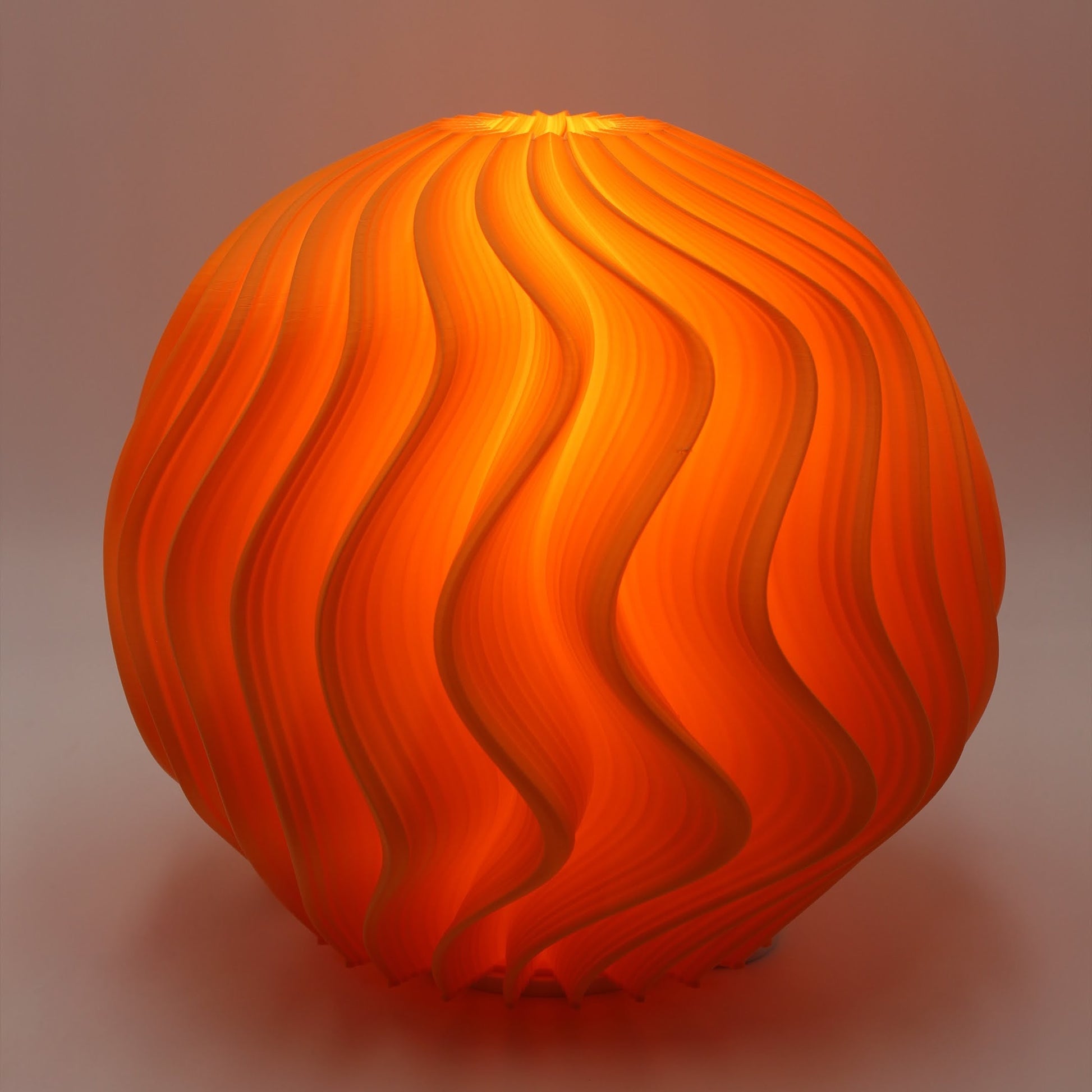 Full studio view of the Flamingo Orb Lamp, showing its curved orb shape and layered wave surface lit in bright orange.