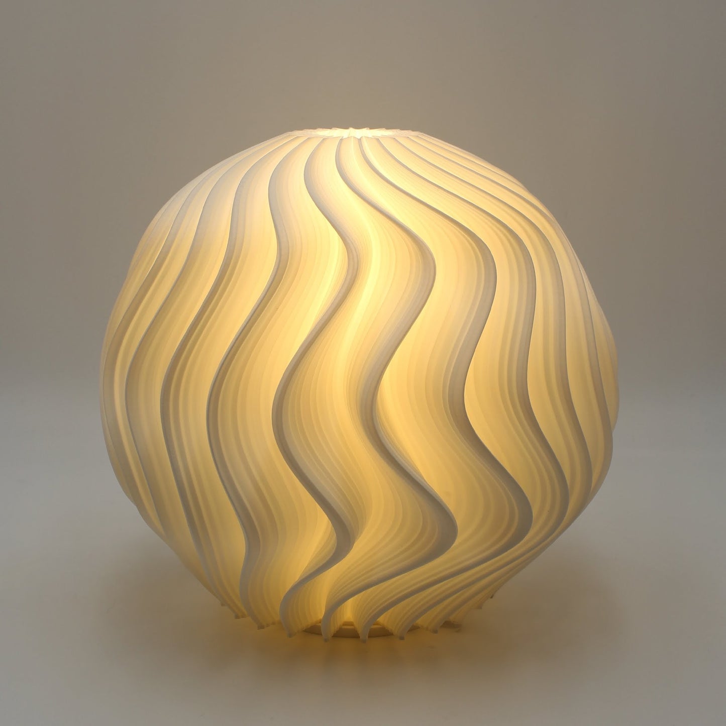 Studio close-up of the White Orb Lamp with its curved wave-like texture illuminated in warm white light.