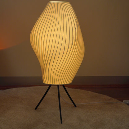 Crème Pleat Floor Lamp switched on, showing its flowing pleated shade and slender black tripod.