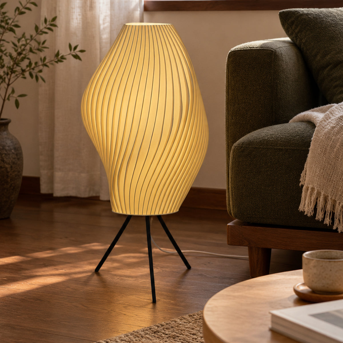 Crème Pleat Floor Lamp illuminated on a black tripod beside a green sofa and timber coffee table.