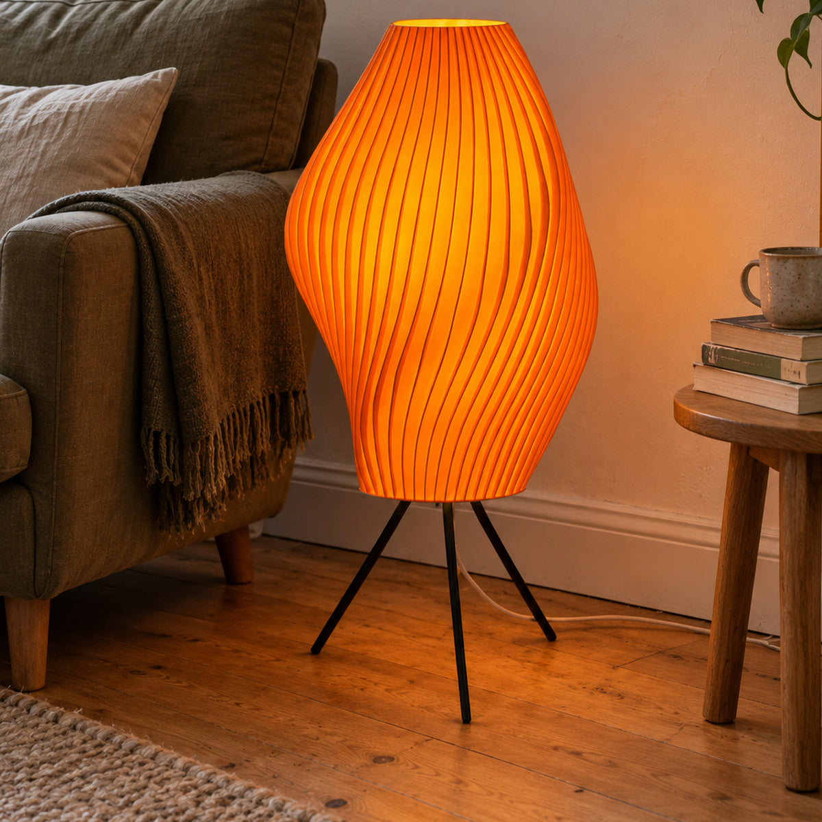 Mandarin orange Pleat Floor Lamp illuminated beside a green armchair in a bright reading nook.
