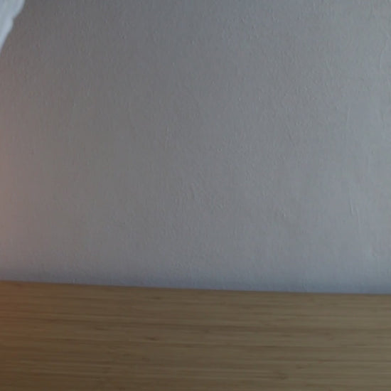 A short, dynamic video showcasing the portability of the cordless Soft Serve Lamp. It's moved effortlessly from a home office desk, to a kitchen counter, and finally to an outdoor balcony at dusk, highlighting its lightweight design and warm, dimmable glow in different settings.