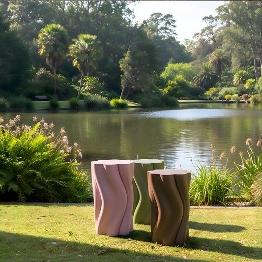 Three wavy-textured outdoor Dune side Tables by a lake with greenery